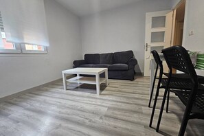 Een kamer met een grijze bank, een witte salontafel en zwarte stoelen.