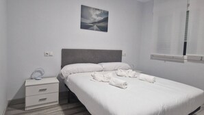 Un lit bien fait, avec du linge de lit et des serviettes blanches, une table de chevet avec une lampe et un tableau accroché au mur.