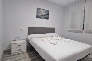 Una cama bien hecha con sábanas y toallas blancas, una mesita de noche con una lámpara y un cuadro en la pared.