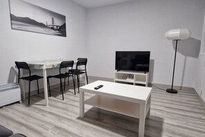A modern living room with a white table, two black chairs, a TV on a stand, and a floor lamp.