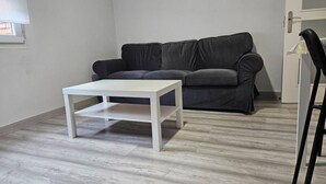 Une pièce avec une table blanche, un canapé gris et une chaise noire.