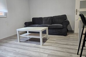 Una habitación con una mesa blanca, un sofá gris y una silla negra.