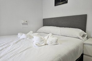 A neatly made bed with white linens and towels, a grey headboard, and a white nightstand with a power outlet. - 1A114 Apartamento moderno de 3 habitaciones (Gijón)