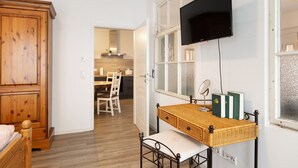 A room with a wooden wardrobe, a wicker desk with books, a television, and a window with frosted glass.