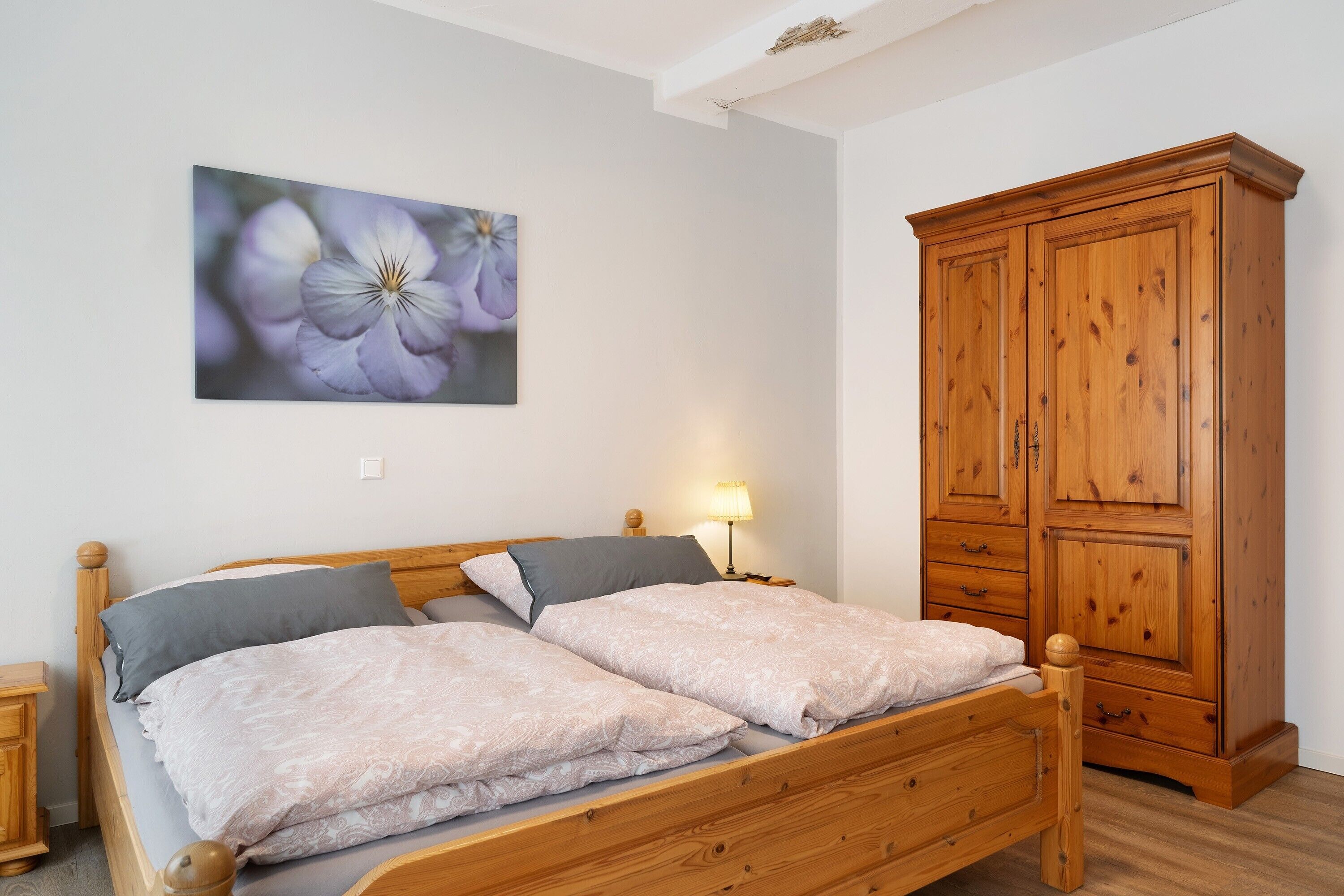 A double bed with a wooden headboard, a nightstand, a lamp, and a wardrobe.