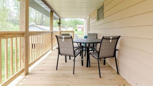A covered porch with a wooden railing, a table with four chairs, and a hanging planter.