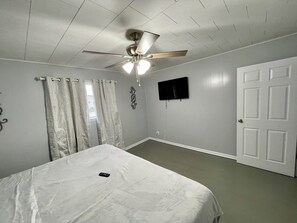 A bedroom with a bed, a ceiling fan, a TV mounted on the wall, and a door. - Cozy Fonzie Flat (Ashland)