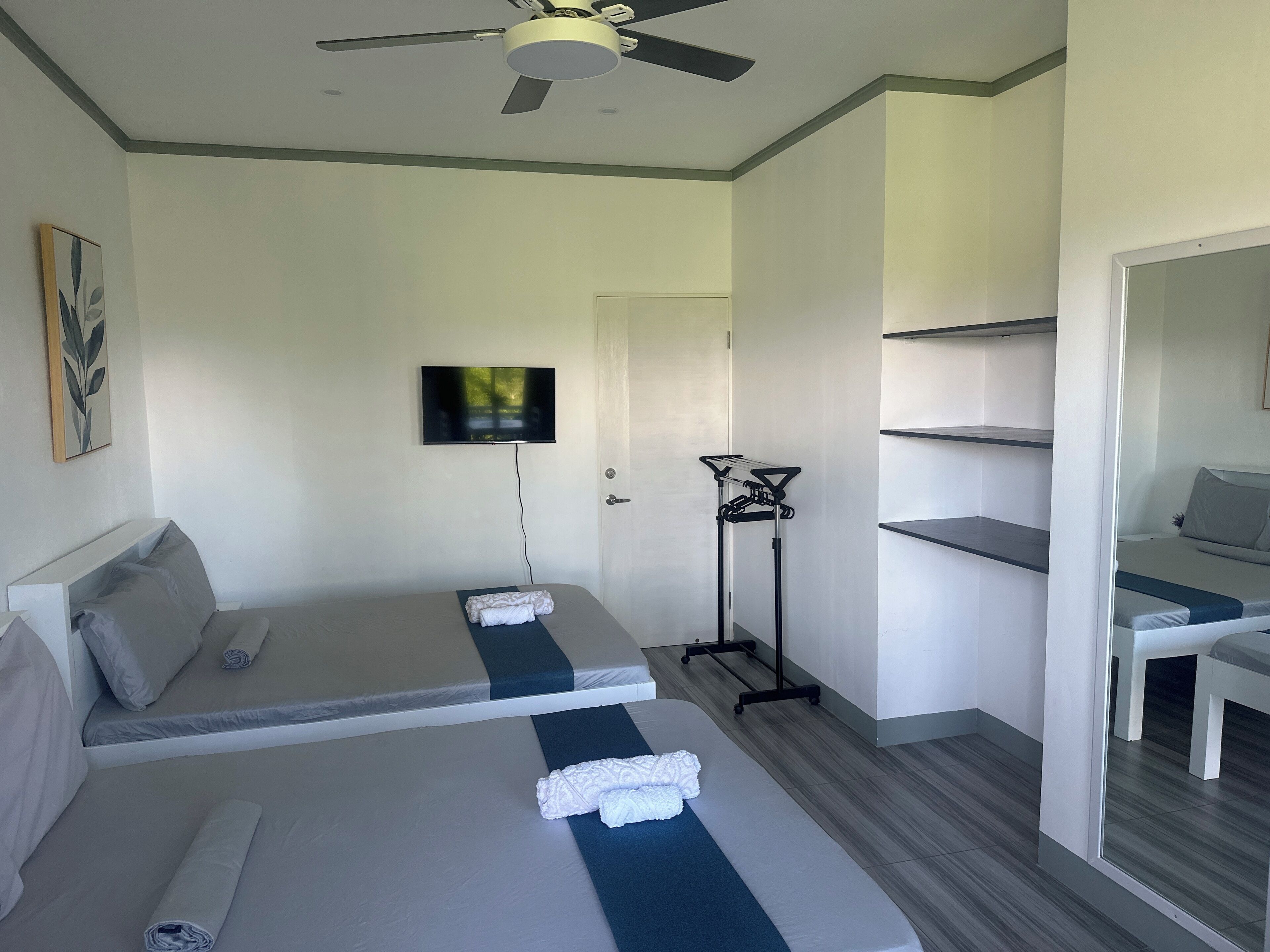 A hotel room with two beds, a TV mounted on the wall, a ceiling fan, and a mirror.
