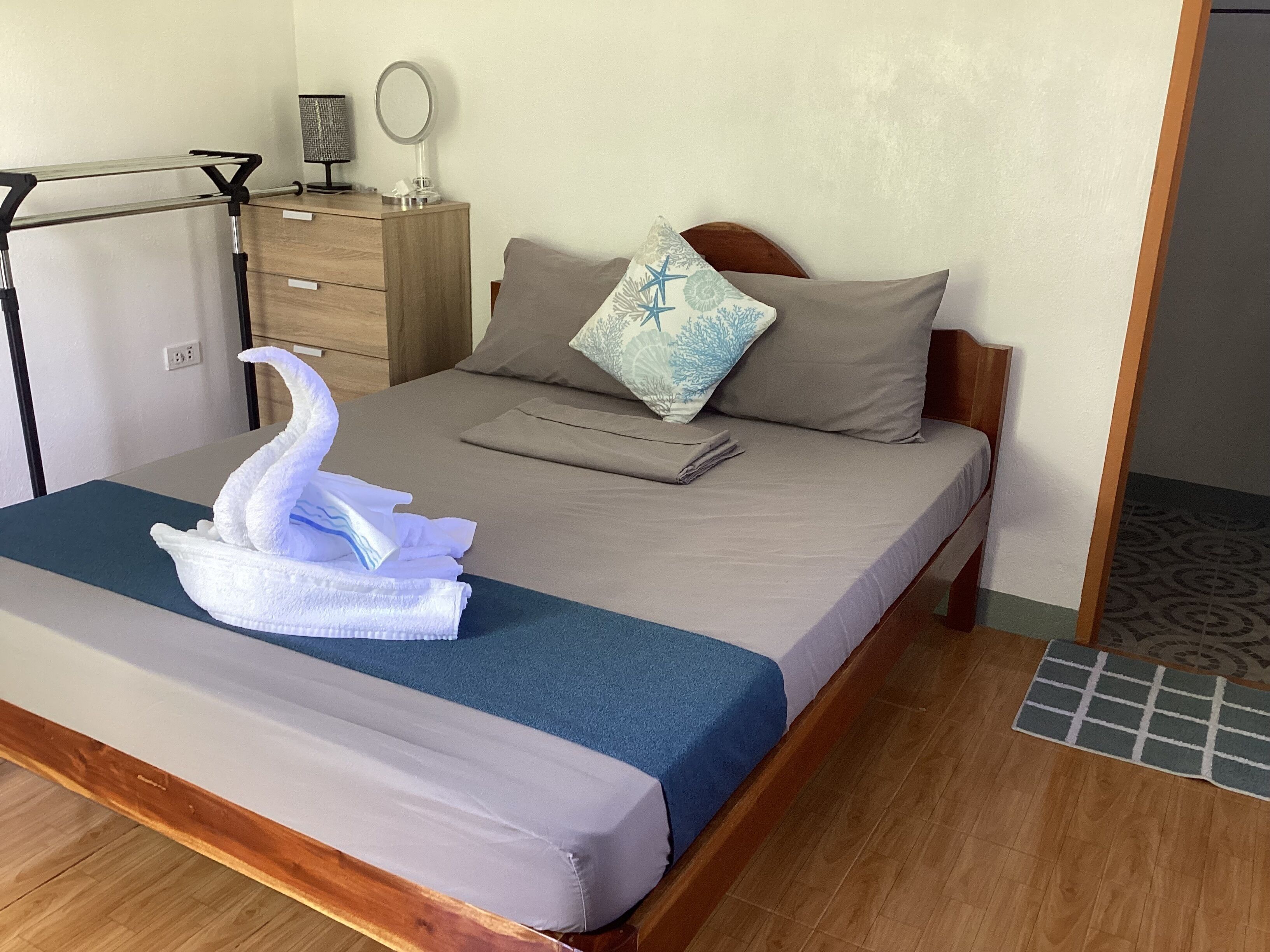 Una cama bien hecha con una colcha azul, un cabecero de madera y una toalla decorativa con forma de cisne.