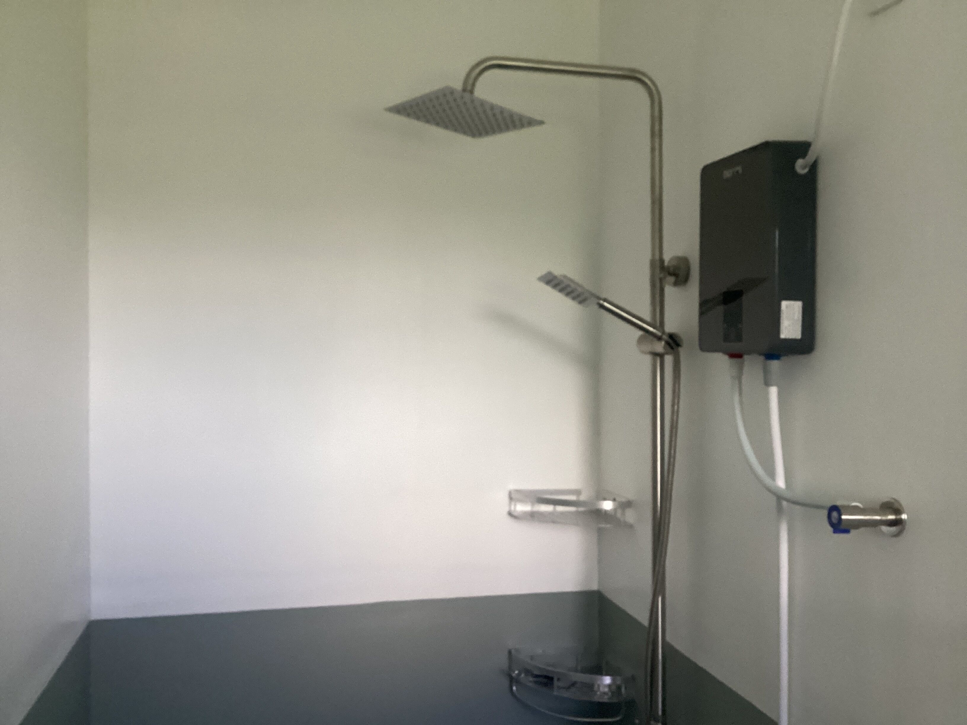 A shower with a handheld showerhead, a wall-mounted faucet, and a control box.