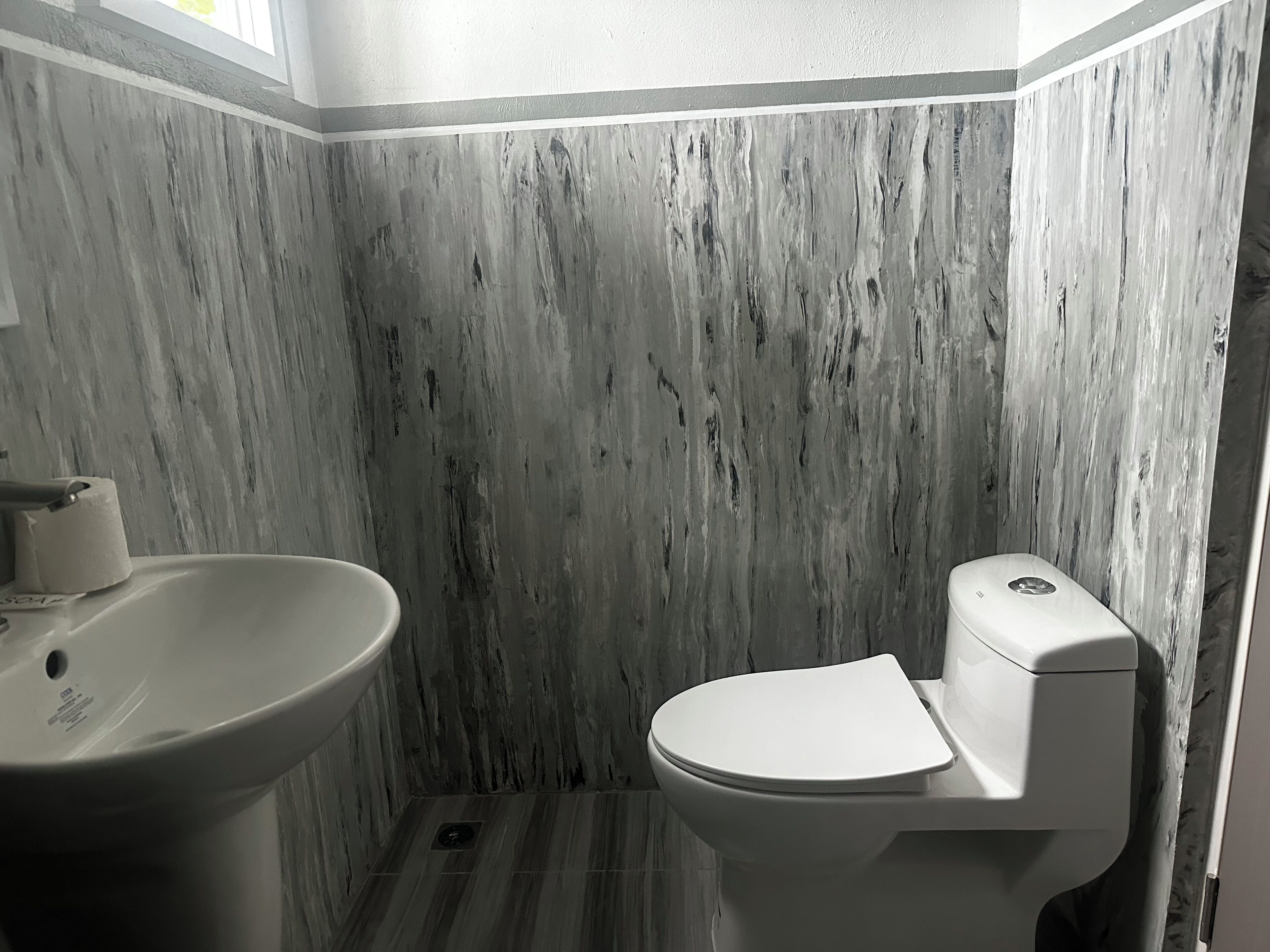 A bathroom with a marble wall, a sink, and a toilet.