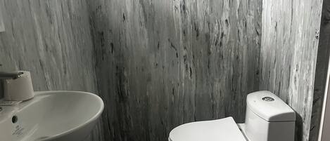 A bathroom with a marble wall, a sink, and a toilet.