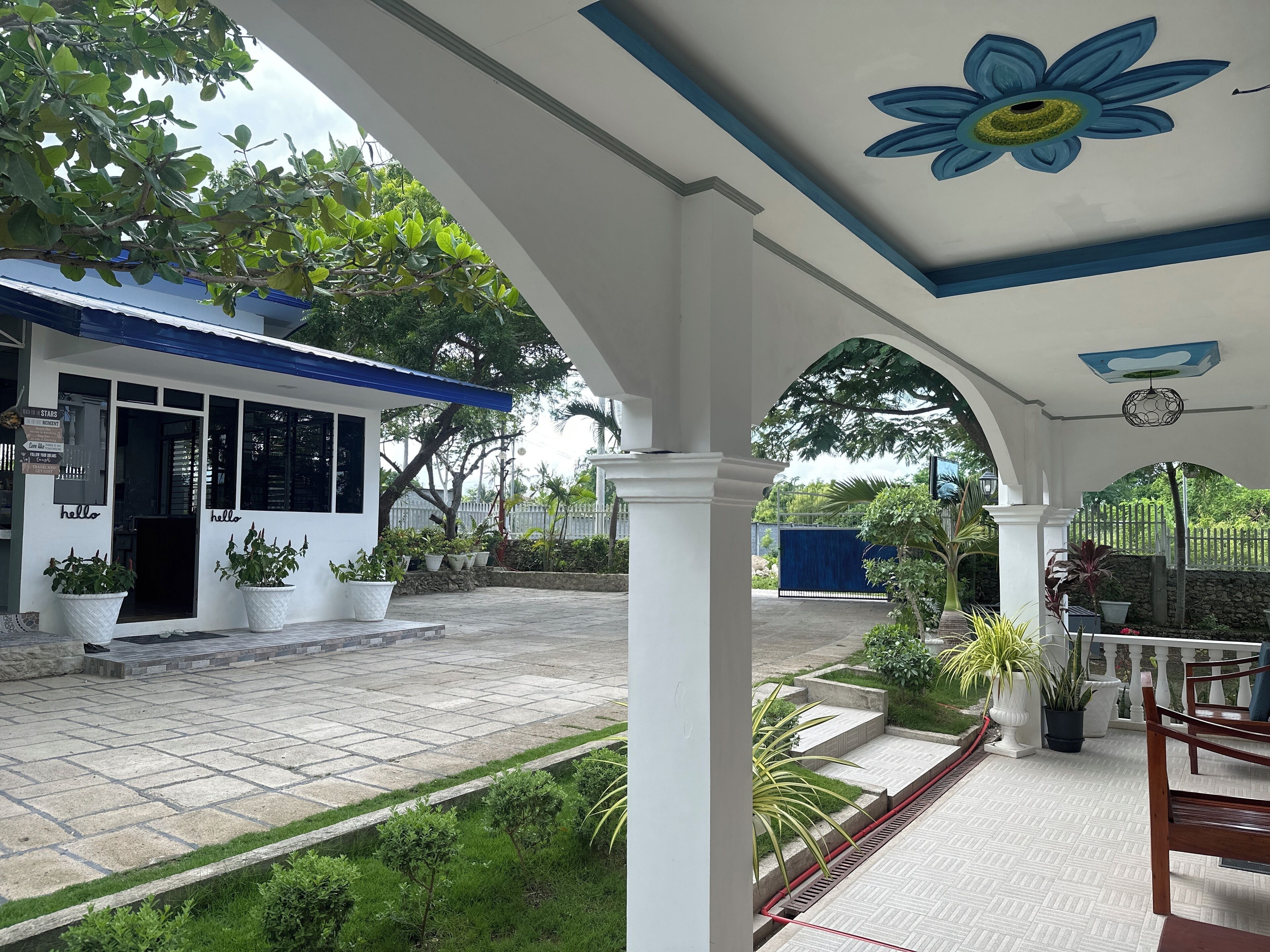 Un espacio exterior cubierto con entrada a un edificio, plantas en macetas y techo decorativo.