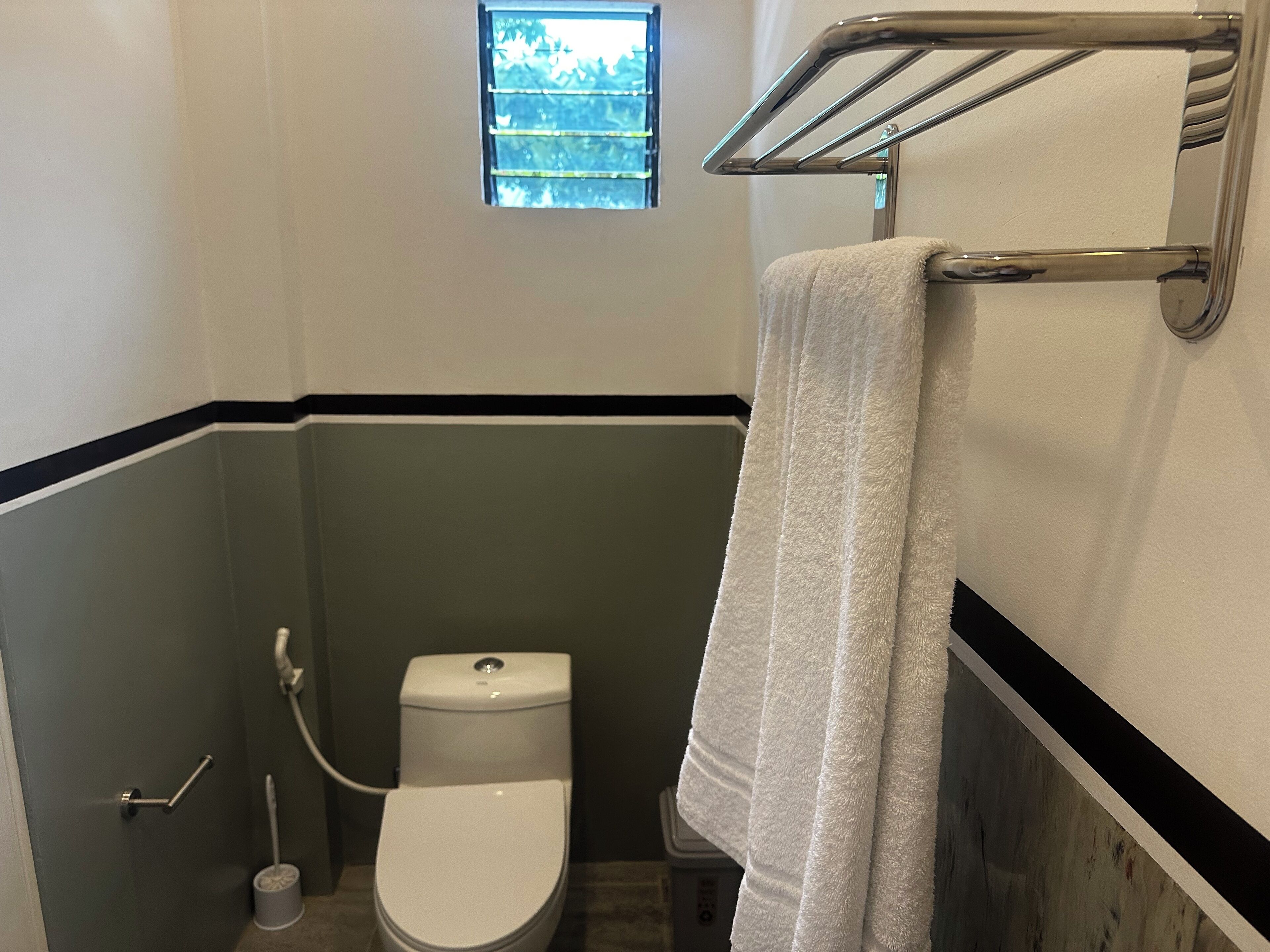 Une petite salle de bain avec des toilettes, un porte-serviettes et une fenêtre.