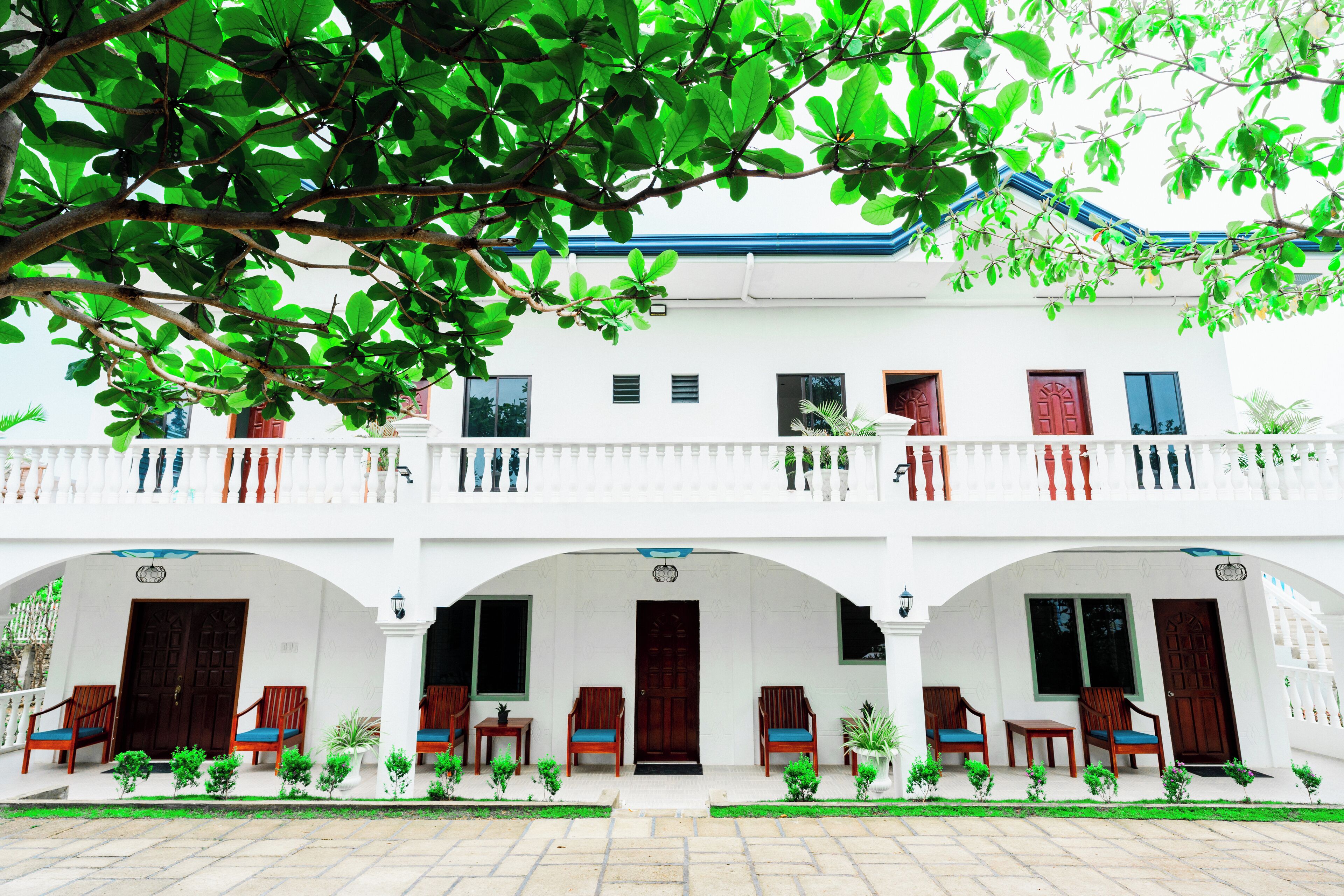 A two-story building with a white facade, multiple balconies, and a series of doors and windows.