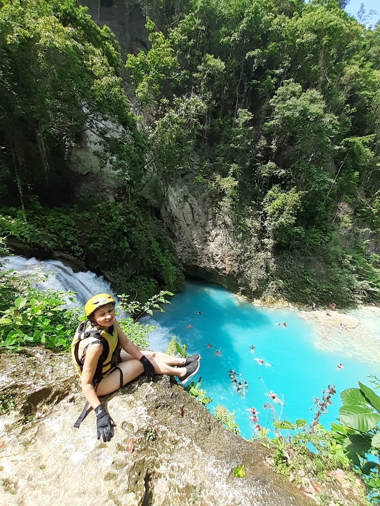 A person sitting on a rock by a clear blue pool surrounded by lush greenery.