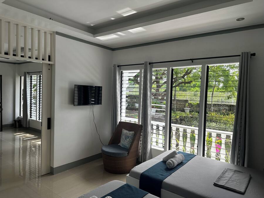 A hotel room with a bed, a chair, a TV, and a large window with a view of greenery.