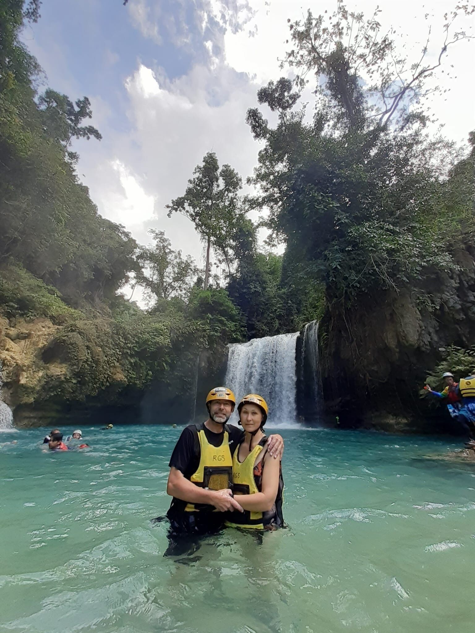 Two people in a natural setting with a waterfall and lush greenery.