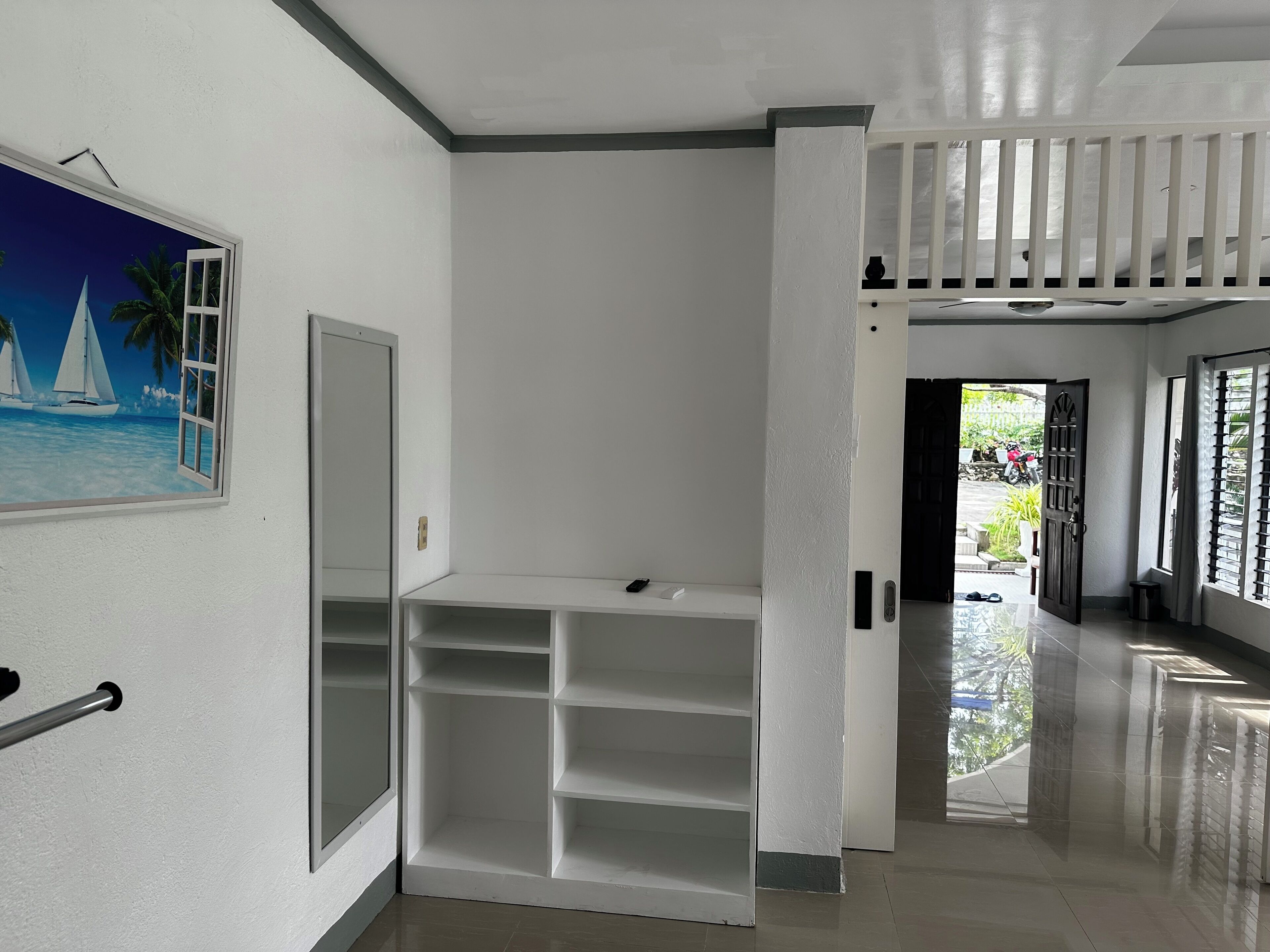 A hallway with a white wall, a door, and a shelf unit.