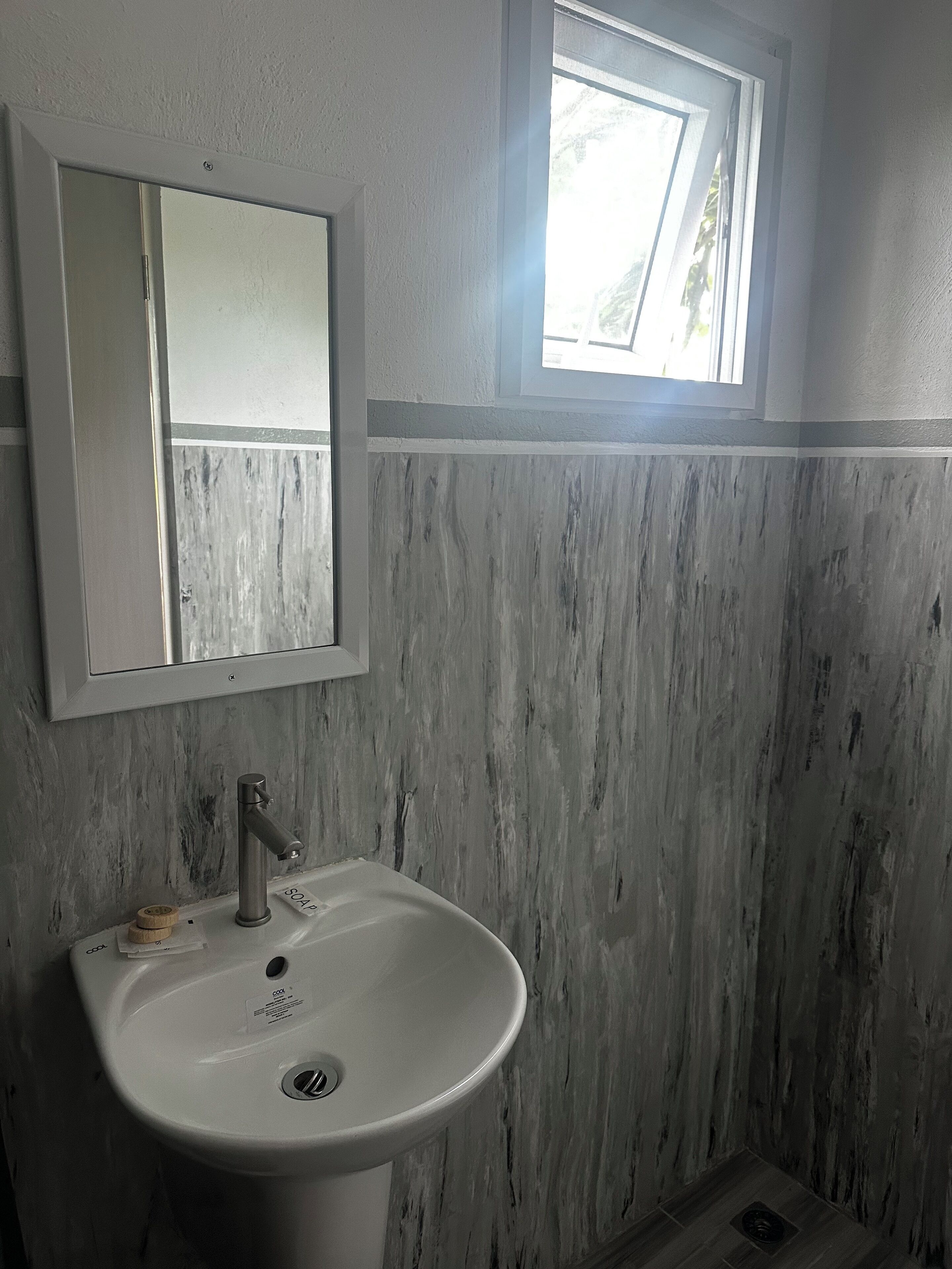 A bathroom with a white sink, a mirror, and a window.