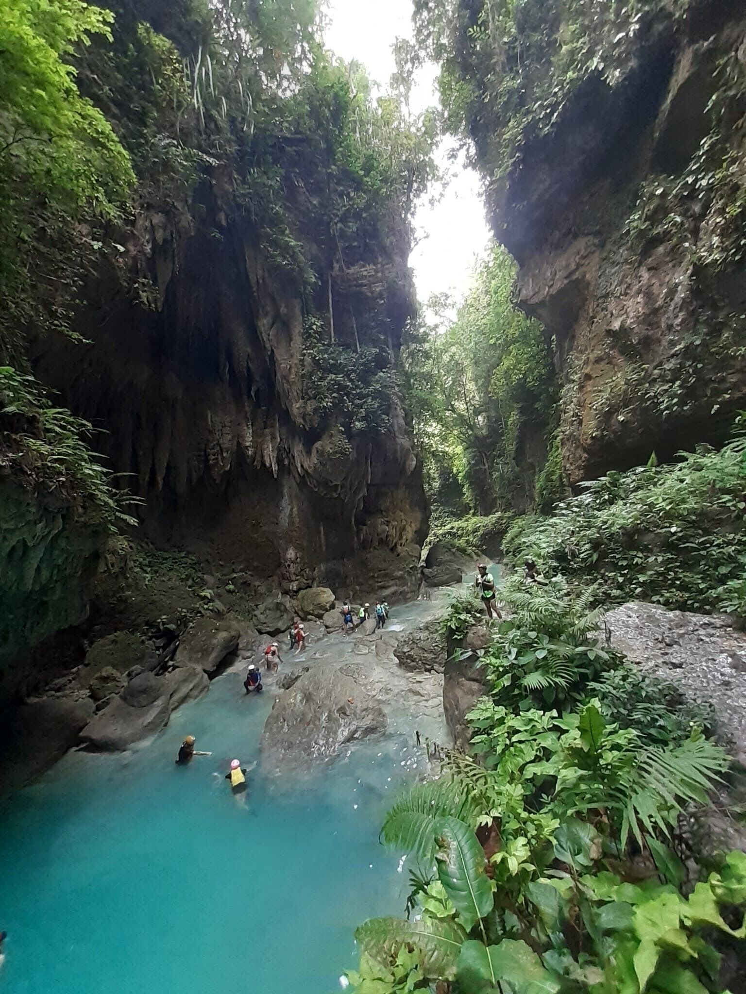 Una cueva natural con una piscina turquesa y terreno rocoso.