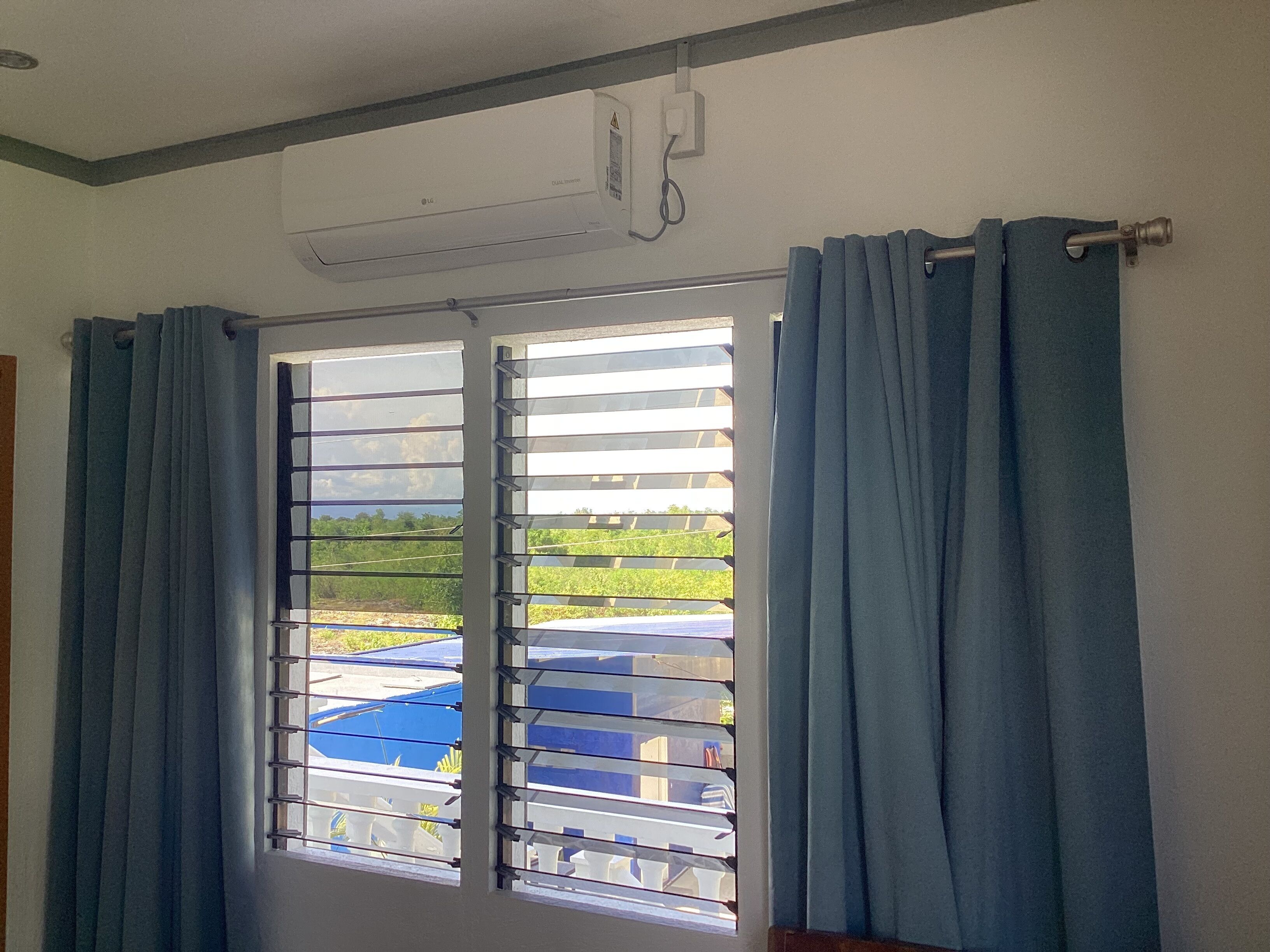 A room with a window featuring horizontal blinds, a ceiling-mounted air conditioning unit, and a curtain rod.