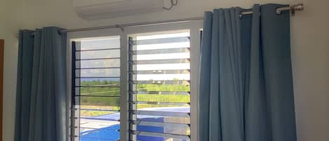 A room with a window featuring horizontal blinds, a ceiling-mounted air conditioning unit, and a curtain rod.