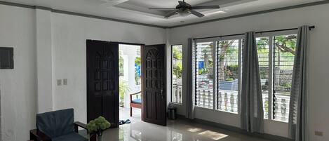 A spacious room with a ceiling fan, large windows with metal bars, a wooden table with a vase, and a chair.