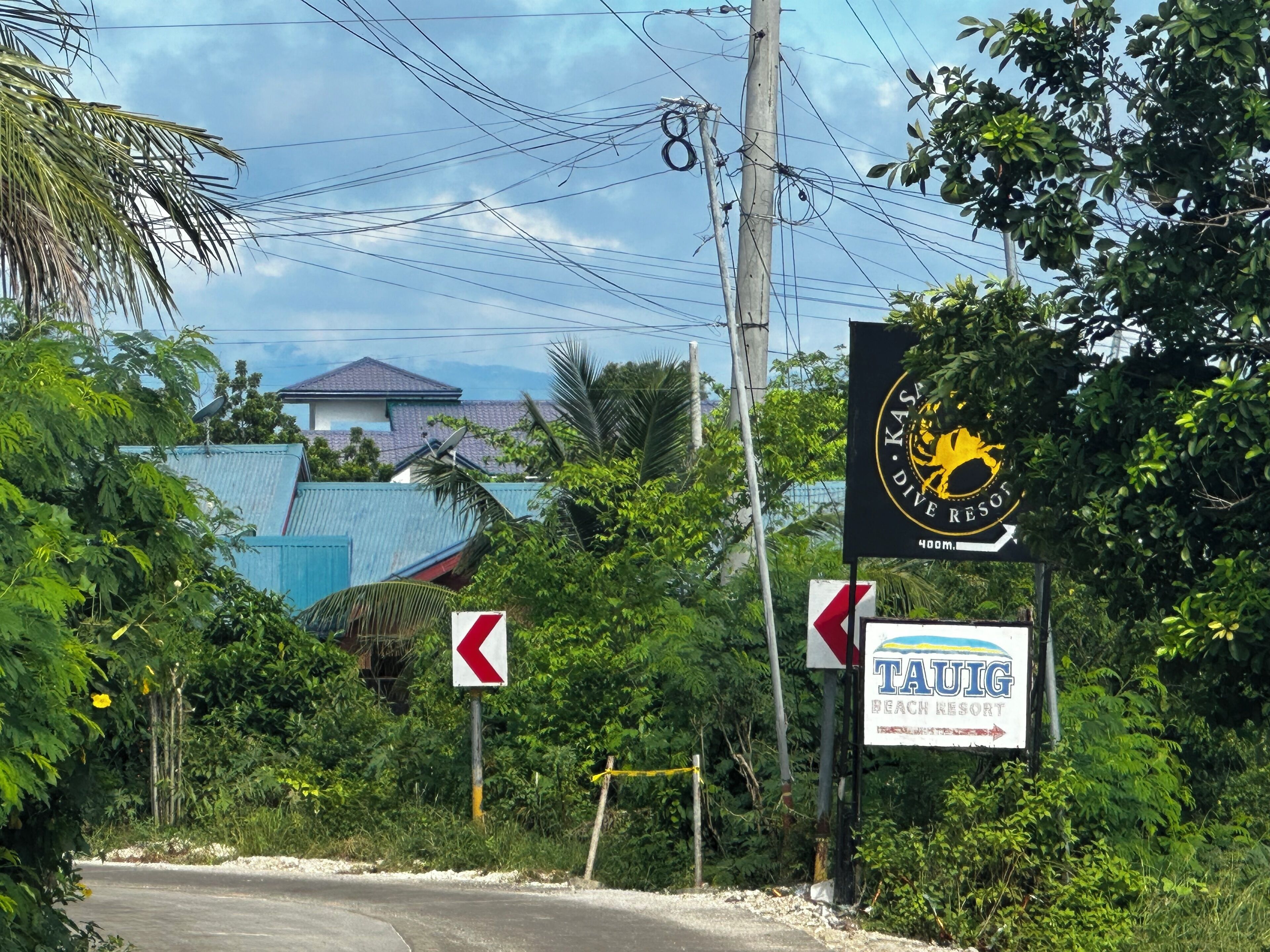 Straßenschild für Kasa Dive Resort und Tauig Beach Resort, mit Pfeil für Abbiegung nach links und einem Pfeil, der nach rechts weist.