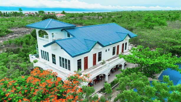 A large, two-story house with a blue roof, surrounded by lush greenery and a view of the ocean. - Moalboal Casablanca Inn  (Moalboal)