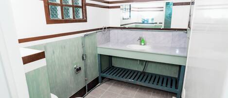 A bathroom with a white toilet, a sink with a green soap dispenser, and a window with a diamond pattern.