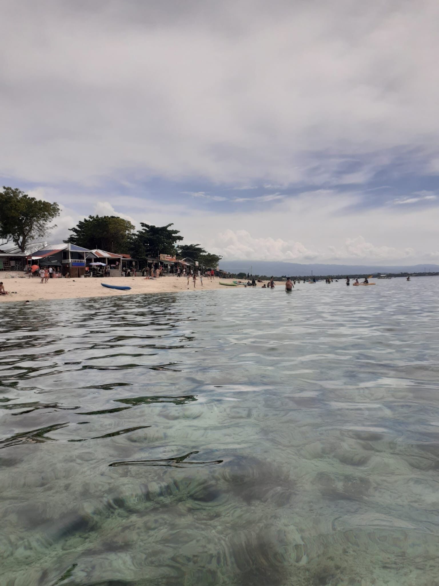 Ein Strand mit klarem Wasser, einem Steg und einem Gebäude mit rotem Dach.