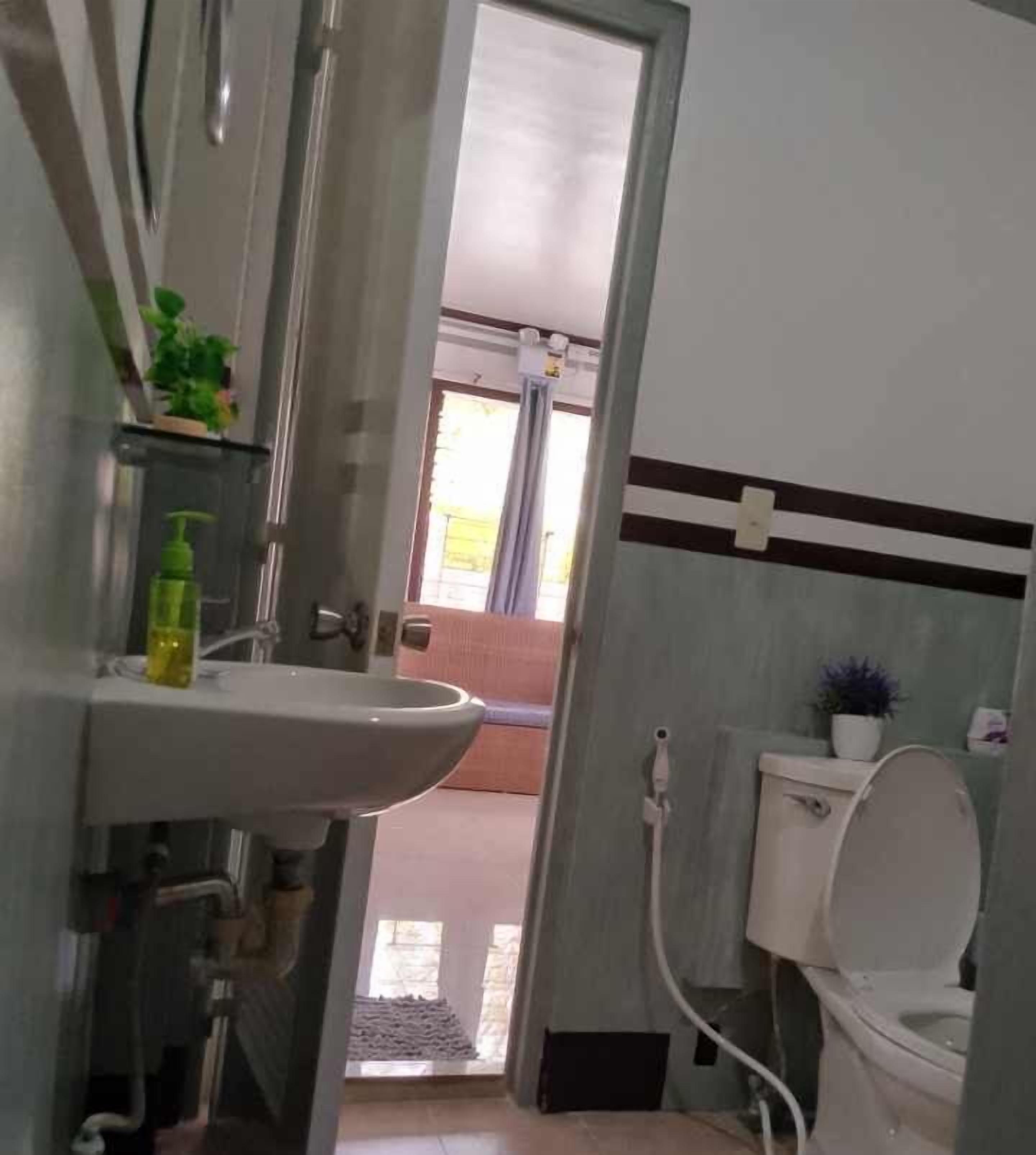 Ein Badezimmer mit Waschbecken, Toilette und einer sichtbaren Duschkabine durch eine offene Tür.