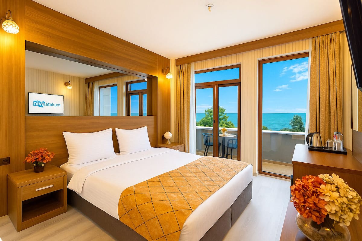 Ein Hotelzimmer mit einem großen Bett, einem Nachttisch, einem Schreibtisch, einem Stuhl und einem Balkon mit Meerblick.