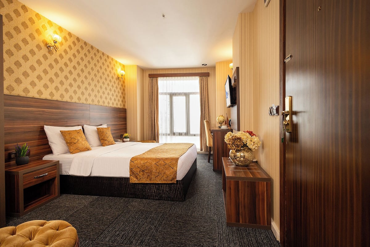 Ein Hotelzimmer mit einem großen Bett, einem hölzernen Kopfteil, einem an der Wand montierten Fernseher und einer Tür mit Griff.