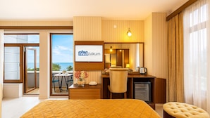 A hotel room with a bed, a desk, a chair, a small TV, and a view of the ocean.