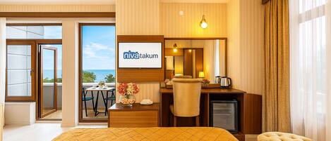 Habitación de hotel con cama, escritorio, silla, un televisor pequeño y vista al océano.