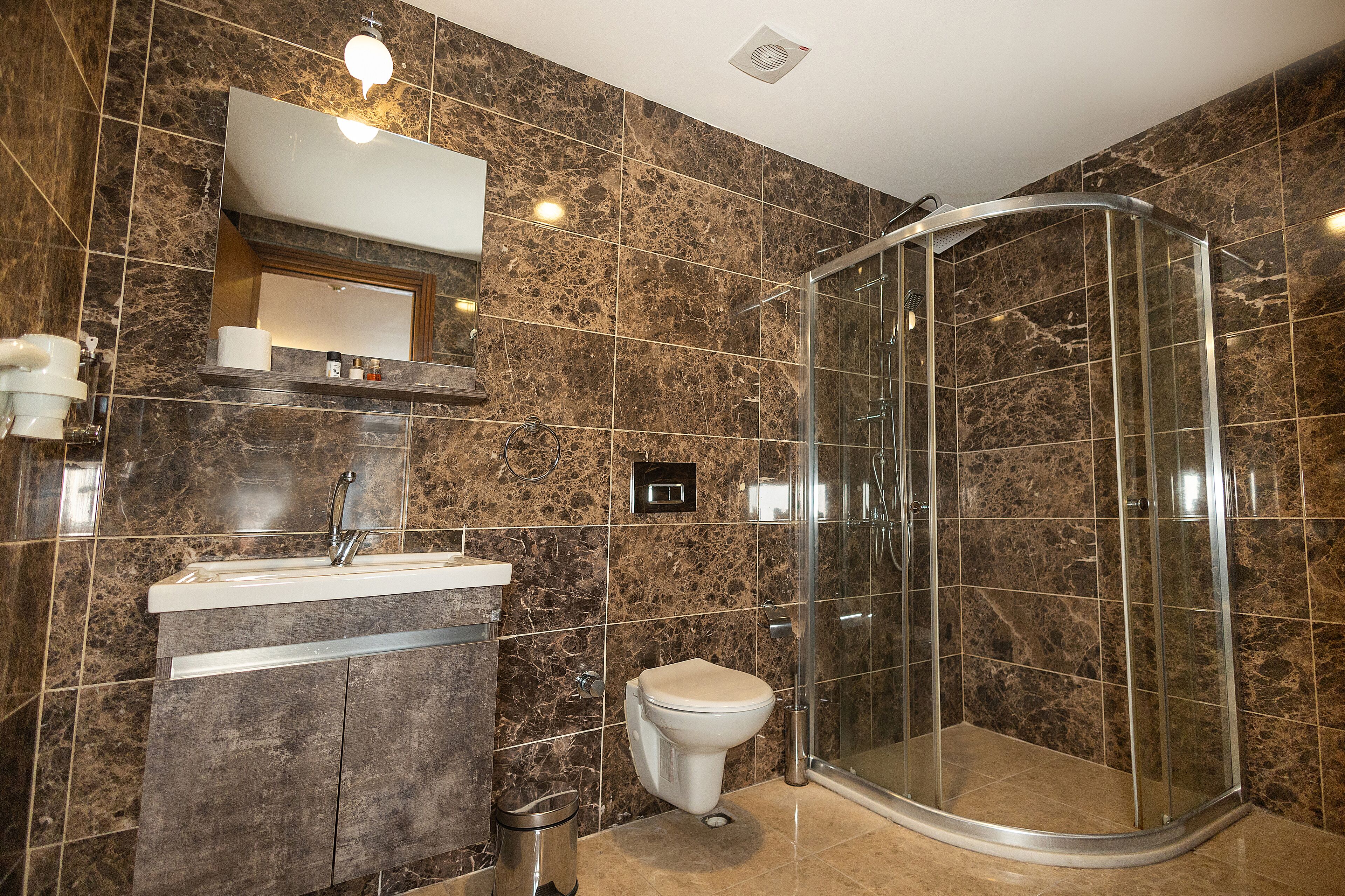 A modern bathroom with a curved glass shower enclosure, a marble-tiled wall, a built-in sink, and a toilet.