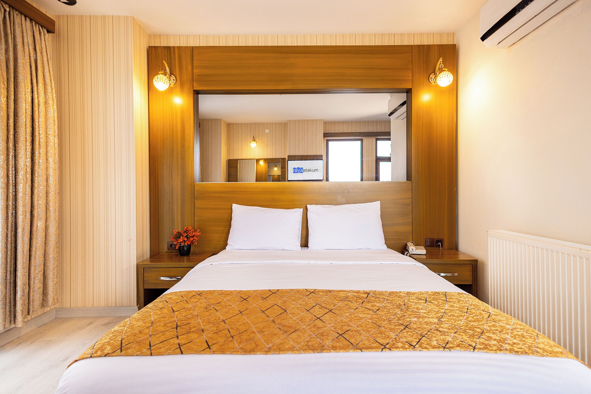 A hotel room with a large bed, wooden headboard, two bedside tables with lamps, a TV, and a view of the city.