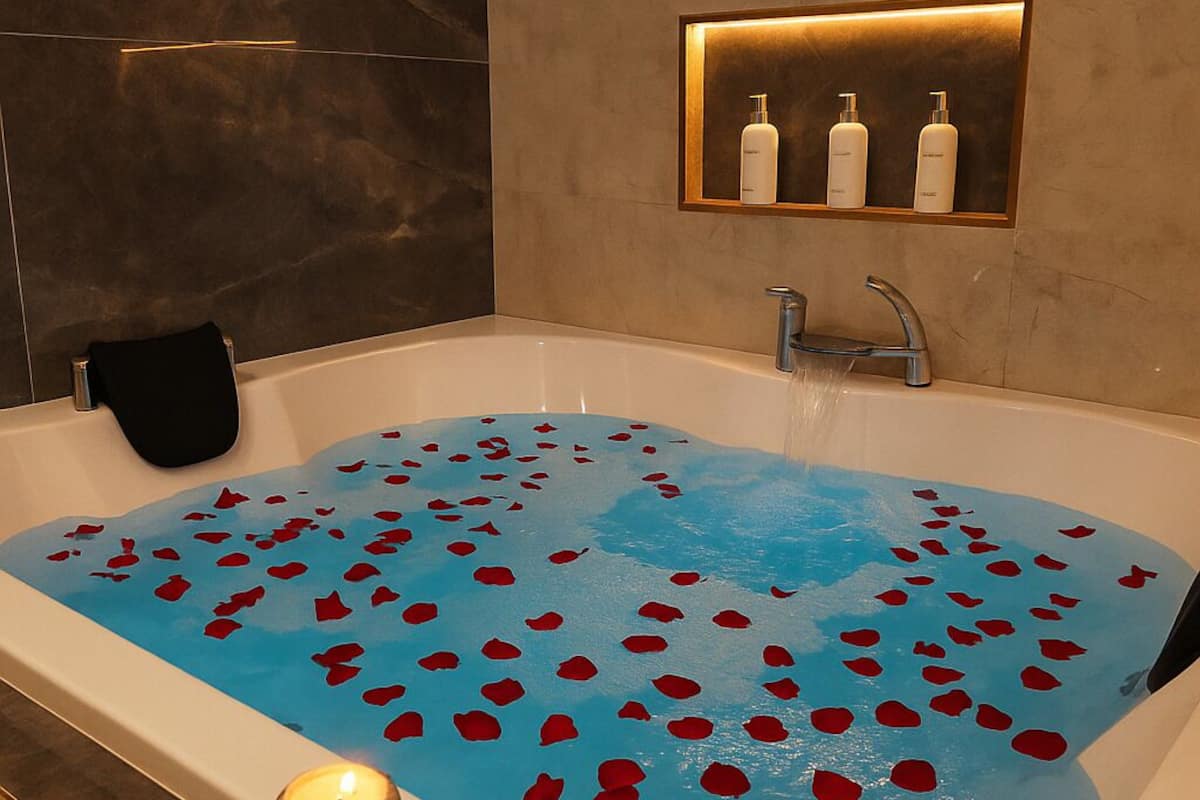 Eine mit Wasser und Rosenblättern gefüllte Badewanne, eine Kerze und ein Spiegel mit Pflegeprodukten.