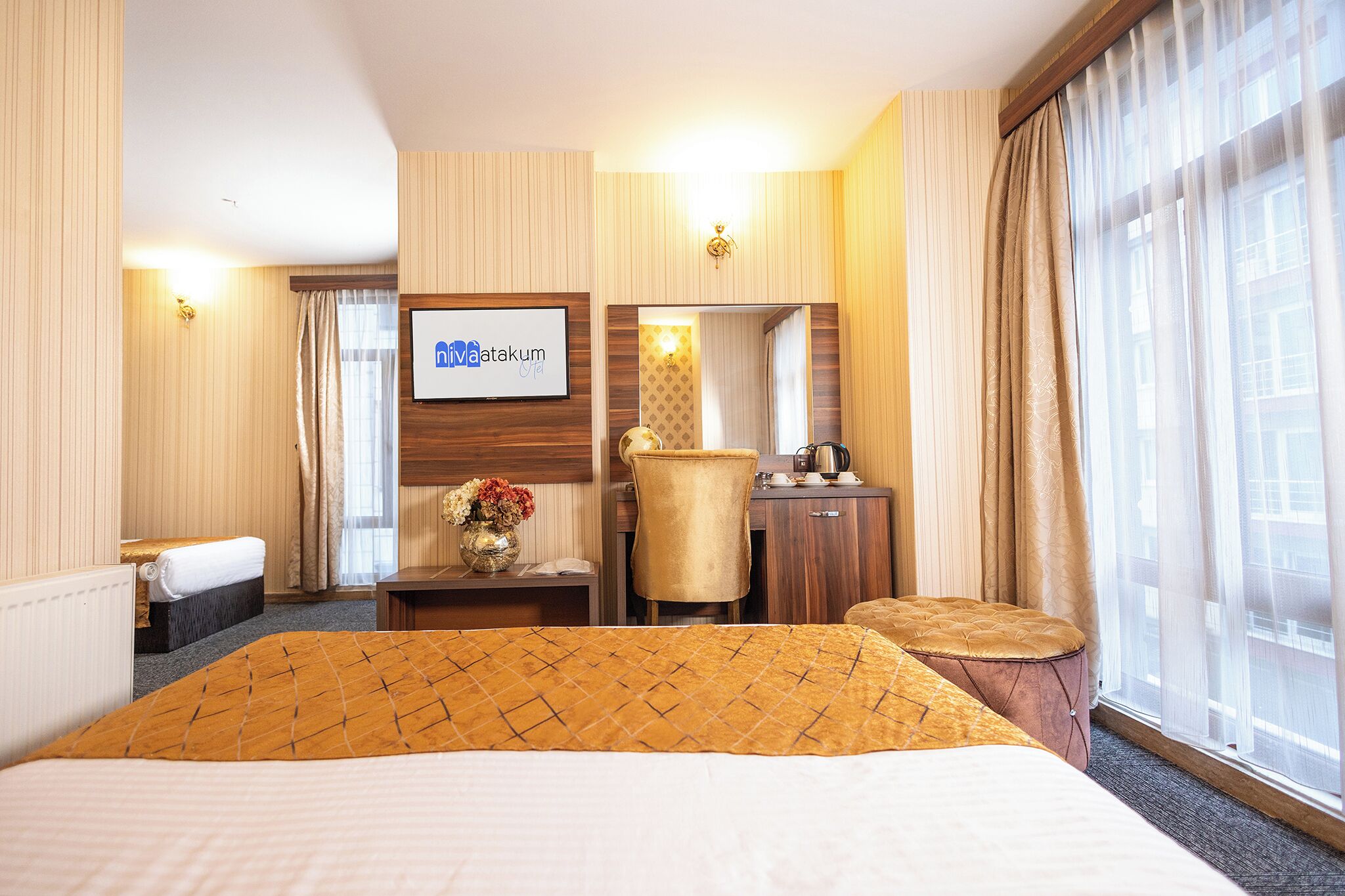 A hotel room with a large bed, a desk with a chair, a small table with a vase of flowers, and a large window with curtains.