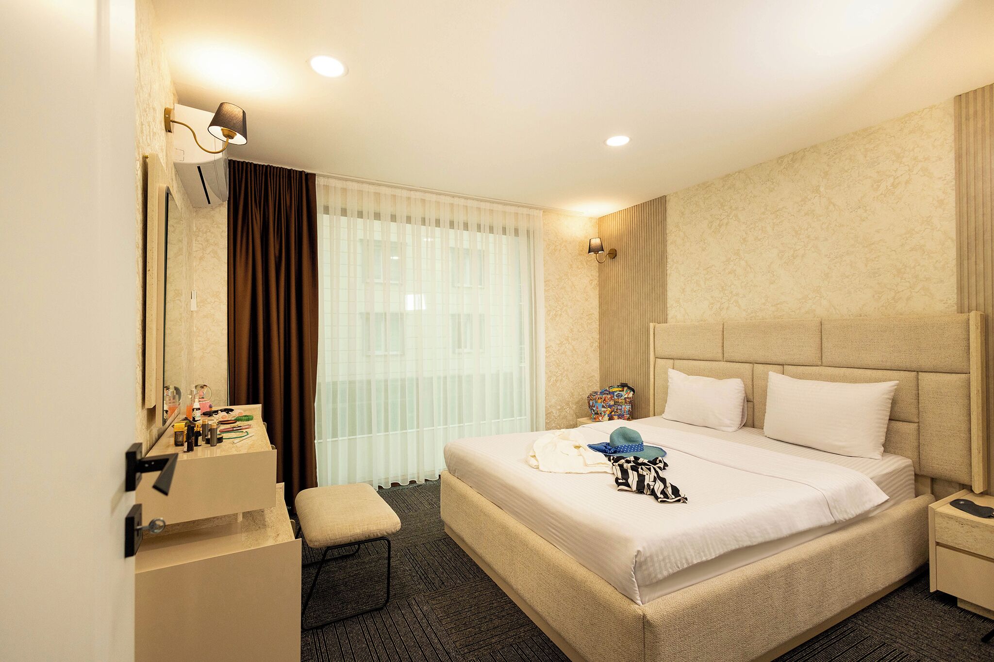 Una habitación de hotel con una cama grande, una mesita de noche, un espejo y una ventana con cortinas.