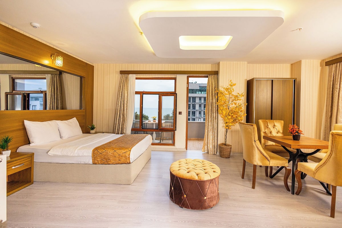 Ein Hotelzimmer mit einem Bett, einem Esstisch mit Stühlen, einem kleinen runden Hocker und einem großen Spiegel.