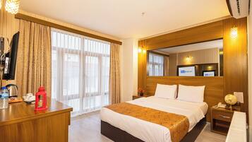 A hotel room with a large bed, a wooden desk, a television, and a minibar.