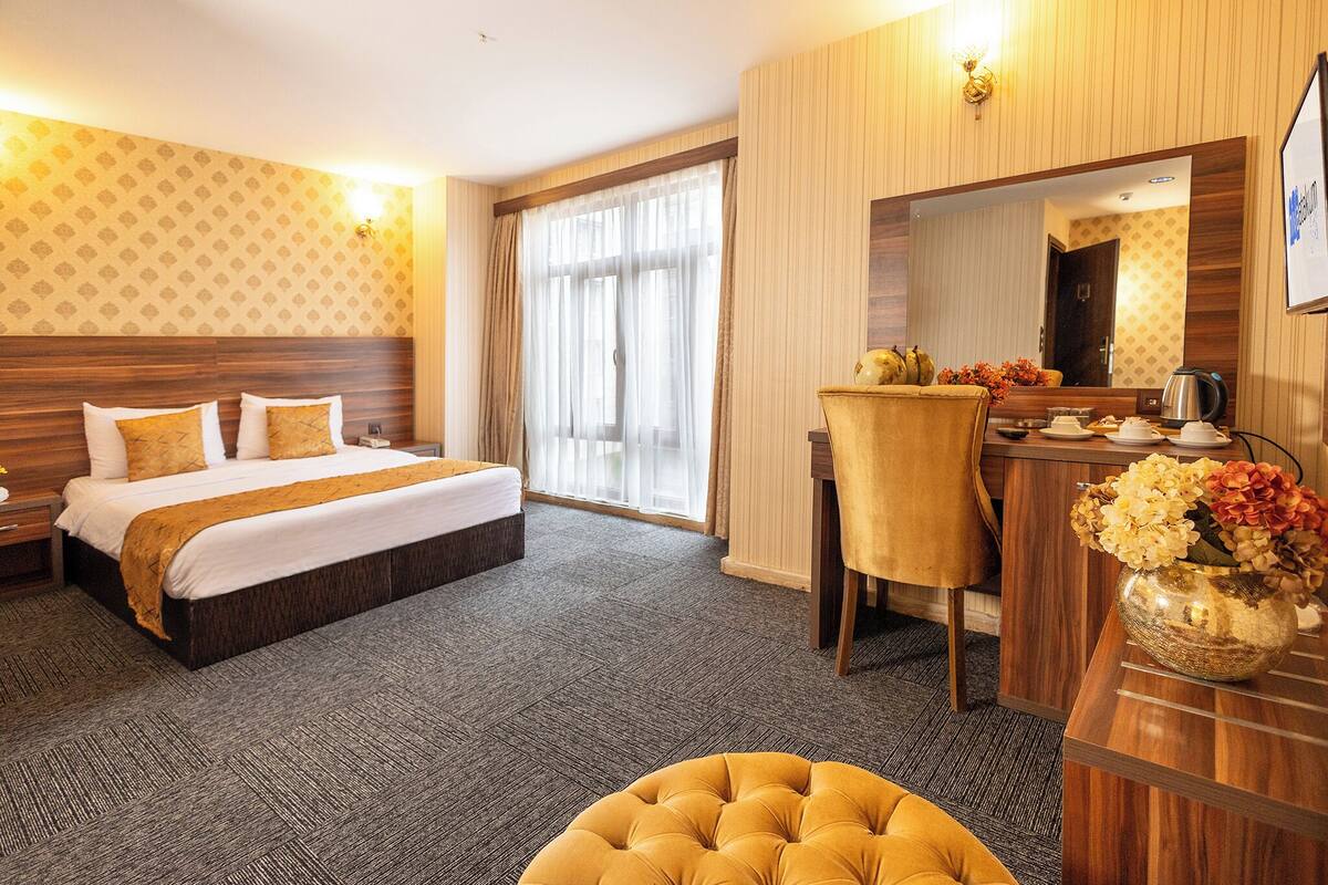 Ein Hotelzimmer mit einem großen Bett, einem Schreibtisch, einem Stuhl, einem Spiegel und einer Blumenvase.