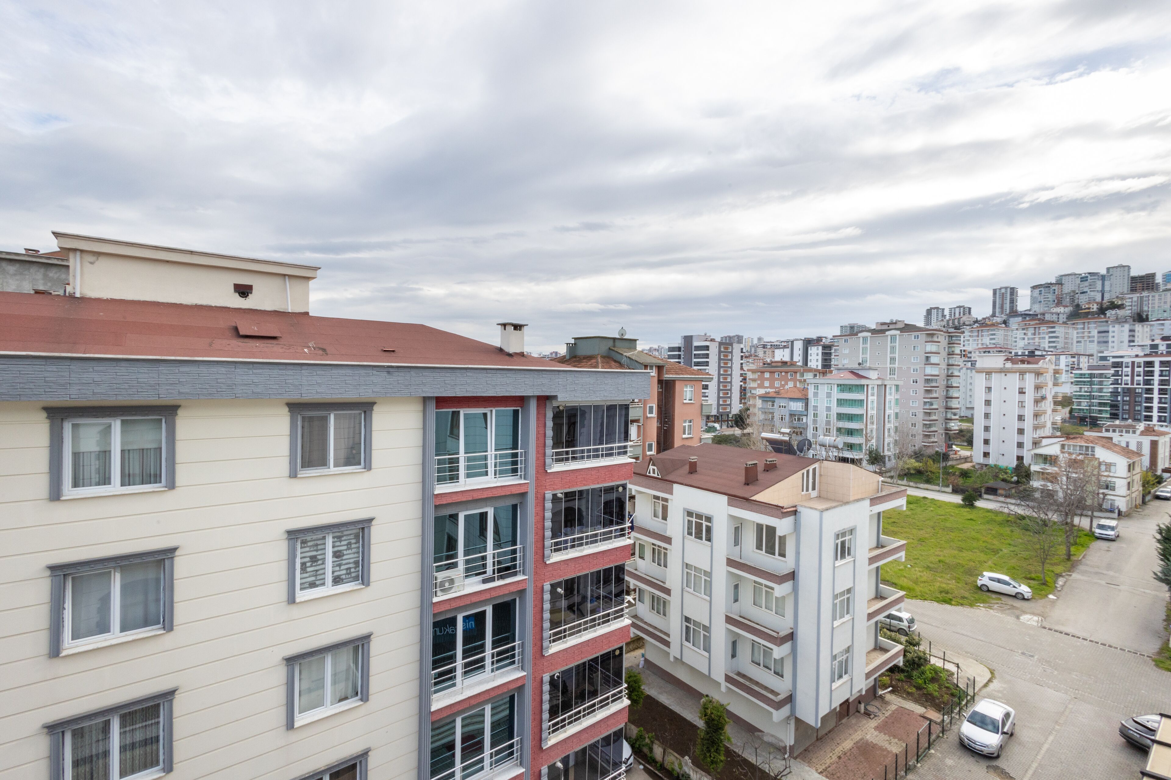A multi-story residential building with balconies, a parking area, and a view of the cityscape.