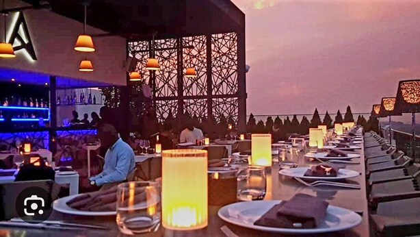 A restaurant with a long dining table, candles, and a bar area in the background.
