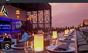 A restaurant with a long dining table, candles, and a bar area in the background. - Aspire Suite - Douglas Luxury Apartments (Accra)