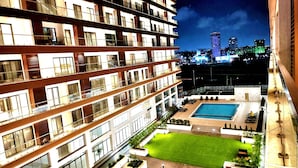 A multi-story hotel with a rooftop pool, a well-maintained lawn, and a cityscape view in the background.