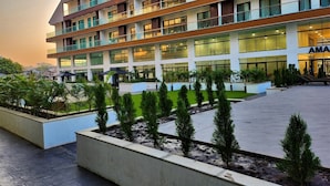 A multi-story hotel with a modern design, featuring balconies, large windows, and a landscaped courtyard with young trees.